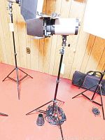 Studio flash light mounted on stand with barn doors and coiled power cable on floor near carrying cases.