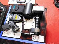 Overview of three camera flashes, Minolta light meter, and lenses on surface with manuals and cases