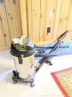 Full view of Stanley wet/dry vacuum with stainless steel tank, black and yellow top, attached hose and wheels.