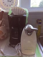 Black Proctor Silex coffee maker with glass carafe, paper filter taped on top, next to white Hamilton Beach electric can opener on kitchen counter