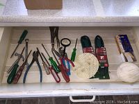 View of an open drawer containing assorted hand tools, extension cords in packaging, white twine, and packing discs arranged neatly on a white tray.