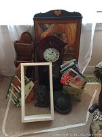 Photo showing a mantel-style clock, black cat sculptures, white frame, DVDs and VHS tapes in floral container, wooden mail holder, and cat calendar.