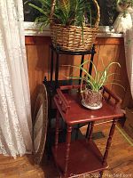 Two plant stands next to a window with live plants on and around them, along with a plastic framed mirror leaning nearby.