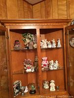Interior view of glass cabinet with assorted figurines including animals, people, and small decorative pieces arranged on glass shelves.