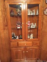 Front view of the wood corner curio cabinet showing glass doors and shelves with collectibles inside.