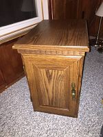 Side view of the wooden side table showing decorative grooved trim, hinged door with brass hardware, and wood grain finish.