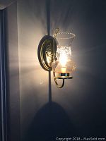 Lit brass wall sconce mounted on the wall showing the light turned on and the shadow it casts.