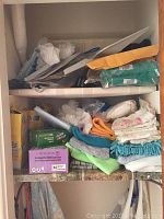 Full view inside cleaning cupboard showing stacked cloths, cleaning gloves, boxes, and cleaning products.