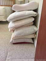 Stack of seven assorted pillows leaning against a wall, showing different shapes and cover fabrics.