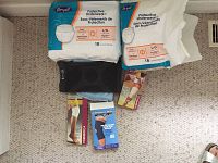 Photo showing two unopened packs of Revel Protective Underwear Large size, a black compression knee sleeve, a knee brace, and a black support belt on carpeted floor.