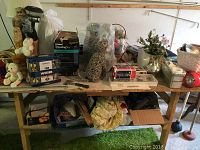 Overview of assorted items on table including plush toys, tools, decorative ceramic animal statue, flower arrangement, boxes, and containers.