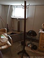 Full view of the wood coat stand in basement setting showing its height and base design.