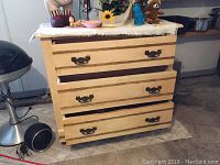 Front view of the small wooden chest of drawers with three drawers, showing brass handles and some wear.