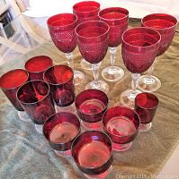 Photo showing 6 red wine goblets with textured diamond pattern on bowl and clear stems, 4 tall solid red glasses, 4 tall textured red glasses, and 1 small double shot glass
