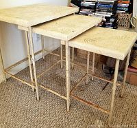 Set of three metal-legged nesting tables with shell imprint tops showing rust on the legs.