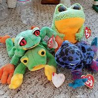 Photo showing all four Beanie Baby frog plush toys displaying their colors and distinct features including red eyes and original TY tags.