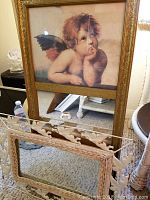 Two cherub mirrors shown; front view focuses on white metal framed mirror with cherub cutouts and partial gold framed mirror behind.