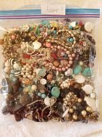 First photo shows a gallon-sized ziplock bag filled with a mixed variety of vintage costume jewelry including bracelets, earrings, and brooches in multiple colors and styles.