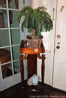 Front view of wooden ornate entry stand with faux palm tree on top against a white door and glass panel.
