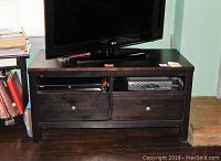 Black wood TV chest with two drawers and two open compartments, holding a flat-screen TV on top.