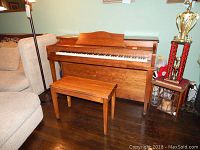 Full view of the Hardman Peck and Co upright piano with bench beside a sofa and floor lamp, showing wood finish and general wear.