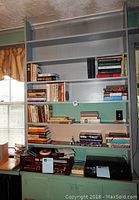 Wide view of bookshelf with various books and two electronic devices below. Books vary in size and color, organized on five shelves.