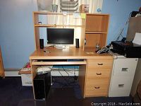 Front view of wooden desk with computer setup showing three drawers, a pull-out keyboard tray, and a detachable bookcase on top with open shelves.