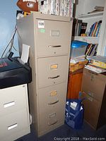 Front-side view of tall beige metal file cabinet with 4 drawers, showing rusted handles and label holders on each drawer.