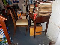 Photo showing the small wood work table with numerous books stacked on top and a red metal vice attached to the side; wooden chair with vinyl cushioned seat positioned next to table