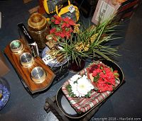 Wooden mounted barometer with three dials, faux flowers in vase and ceramic container, blue decorative plate, and wooden wine rack in the background.