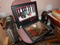 Two framed music-themed wall art sitting on a chair, showing the full artworks including a rose on piano keys and band instruments.