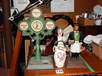 Vintage Dubonnet bar clock with advertising and wired base shown with rye decanter and bartender figurine