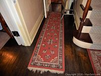 Long red floral runner rug 22x88 inches placed in hallway, showing wear and fringe at ends.