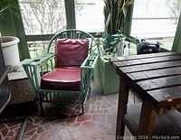 Rattan armchair with red vinyl cushions and part of adjacent wooden potting table on a tiled porch floor.