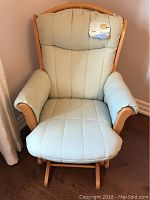 Frontal view of the padded soft green and white checked glider rocking chair with light wooden frame showing the seat, backrest, and armrest cushions.