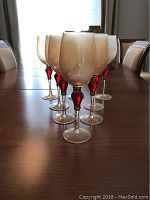 Front view of 8 gold frosted wine glasses with gold and ruby decorated stems on wooden table.