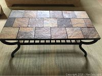 Photo showing the rectangular coffee table with a stone tile top and wrought iron legs on carpeted floor.