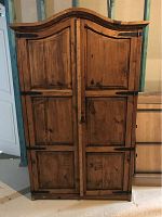 Front view of closed rustic wooden wardrobe with iron hinges and curved top molding