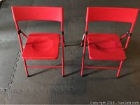 Two red kids folding chairs shown from front on a dark foam mat surface.