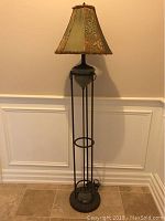 Full view of wrought iron floor lamp with decorative fabric shade against beige wall and tile floor