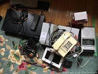 Wide view of all items included in the lot on a floral carpet. Shows Panasonic DVD player, telephone, digital photo frame, Pulser cassette recorder, various cables and power adapters.