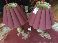 Pair of lamps with burgundy shades and metallic finish bases placed on a carpet, showing pleated and scalloped lamp shades.