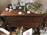 Wooden buffet shown with various decorative items on top including brass candlesticks, china cups, and figurines.