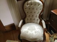 Front view of a single parlour chair showing cream button-tufted backrest and patterned fabric seat with carved wood frame and arms.