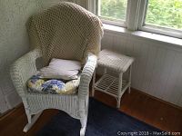 White wicker rocking chair with floral seat cushion, zebra cushion, and cream crochet throw, set near wall and window.