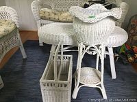 Overview of white wicker coffee table, magazine rack, plant stand and plant pot grouped together on blue carpet