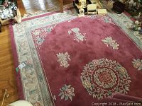 Full view of the rose-colored floral area rug with decorative border on hardwood floor.