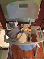Plastic bath chair loaded with health and personal care accessories: blood pressure monitor, cuff, soap, comb, hairbrush, nail clipper