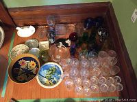 Wide assortment of clear and colored glassware including bowls and plates on floor corner