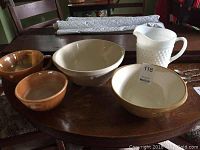 Four bowls and one milk glass hobnail pitcher arranged on wooden table, showing size and finish of items.